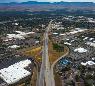 Aerial view of Interstate 84 at the Eagle Road interchange in Meridian, with looping entrance and exit ramps, surrounding businesses and neighborhoods, and the Boise Foothills in the distance.