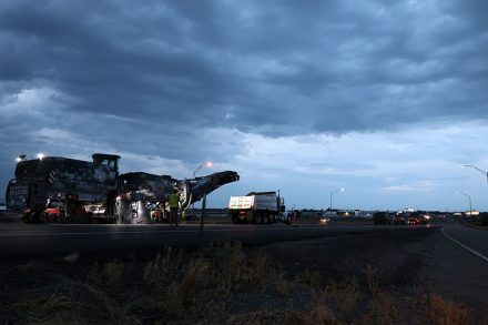 Night work on US-20 near Idaho Falls, showing heavy milling equipment, dump trucks and traffic control devices in a work zone.