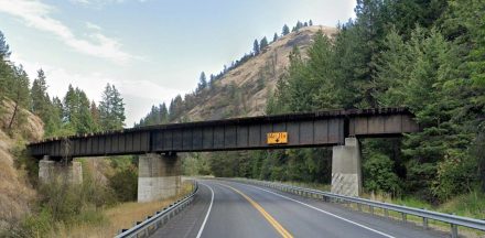 Steel railroad trestle spanning U.S. Highway 95 in Lapwai Canyon. The bridge is supported by three concrete piers, with a 14-foot, 11-inch clearance sign mounted at the center span above the two-lane highway.