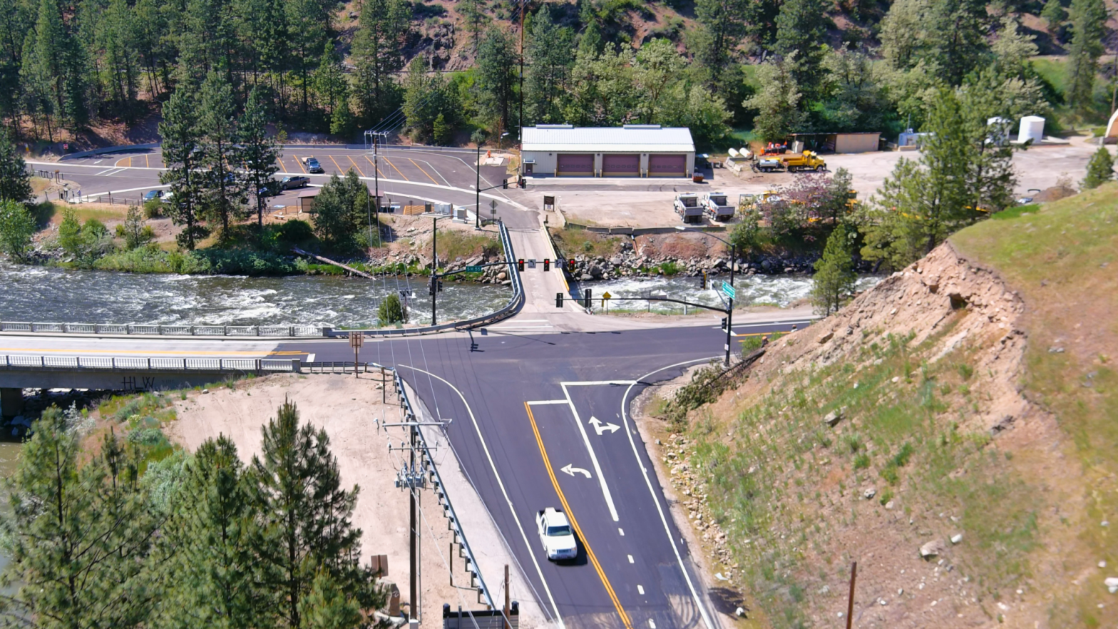 Two two-lane roads cross with a river on one side with a mountain on the other side.