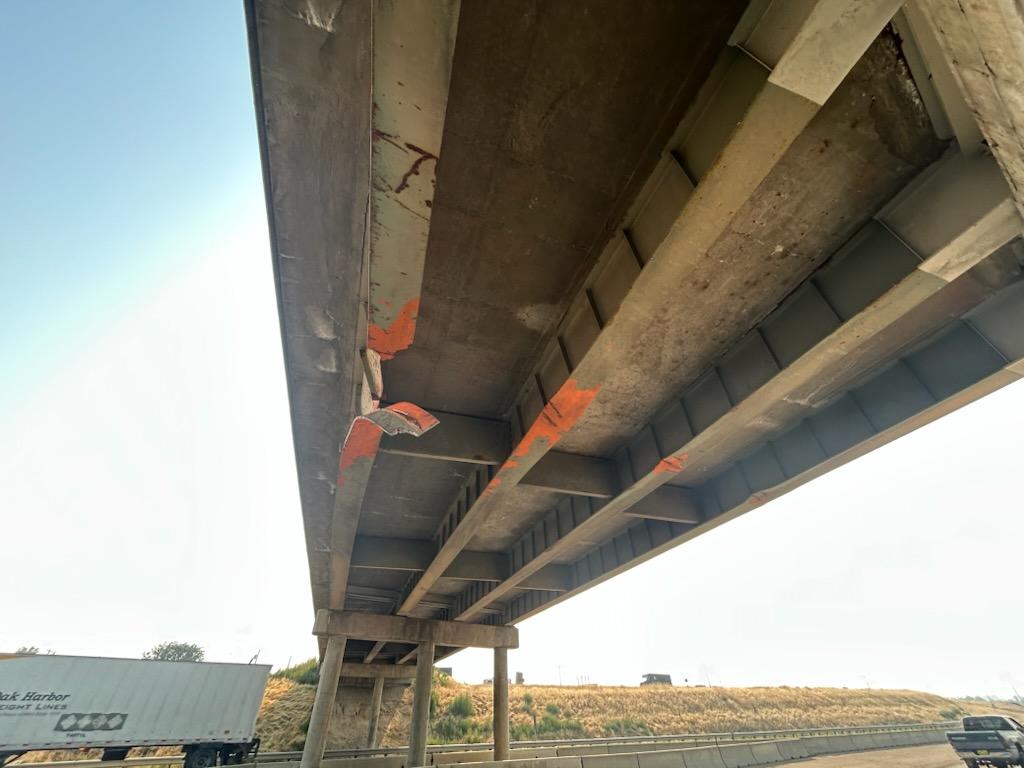 Bridge damage with metal girder hanging from bottom of bridge.