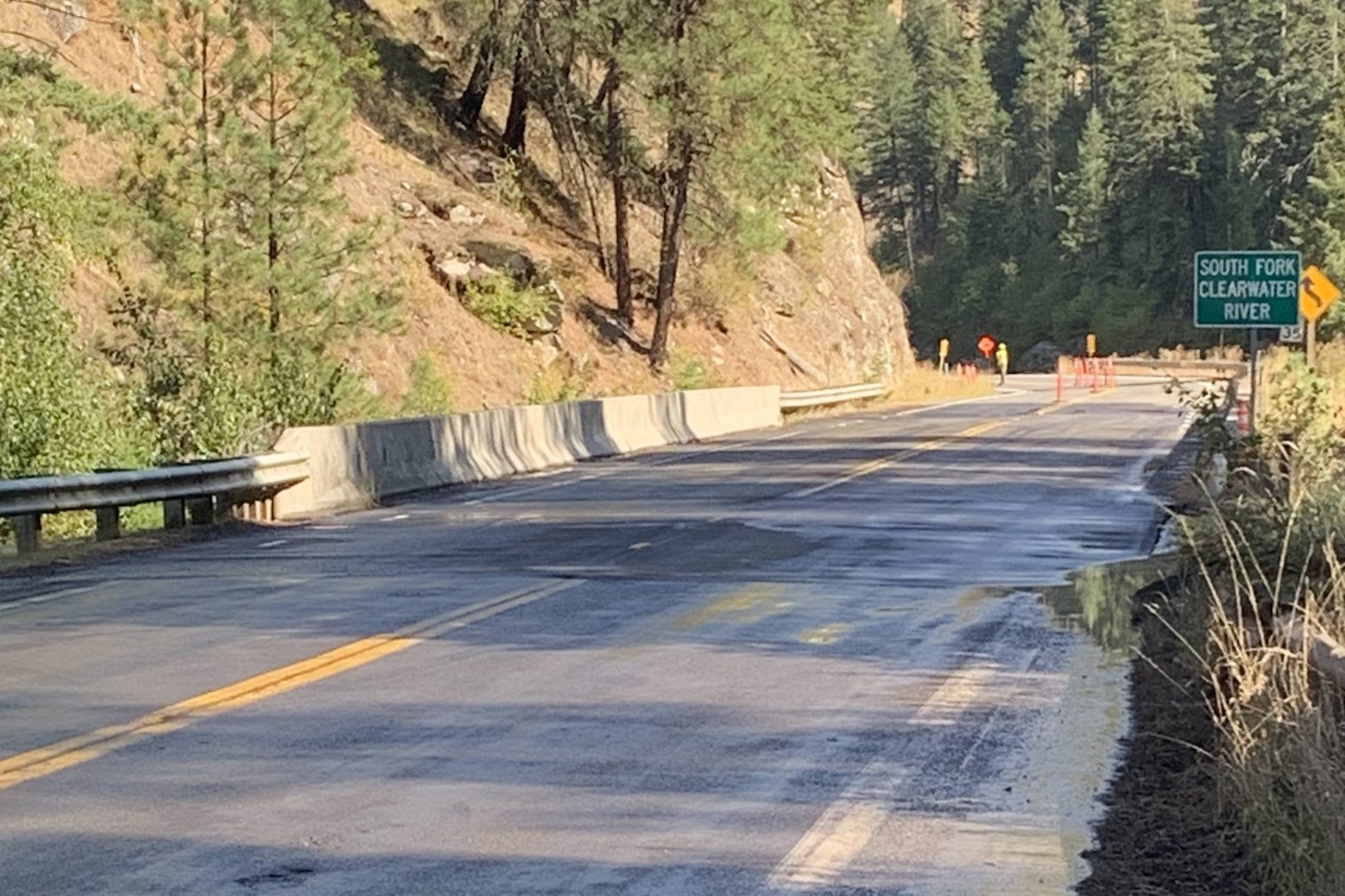 State Highway 14 curves through a forested canyon near the South Fork Clearwater River, with concrete barriers and traffic-control cones along the roadway.