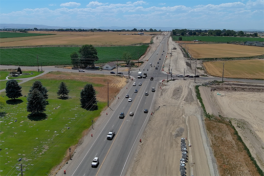 Aerial view of construction at State Highway 55 and Indiana Avenue, with traffic traveling beside excavated areas for road widening. Farmland borders the highway.