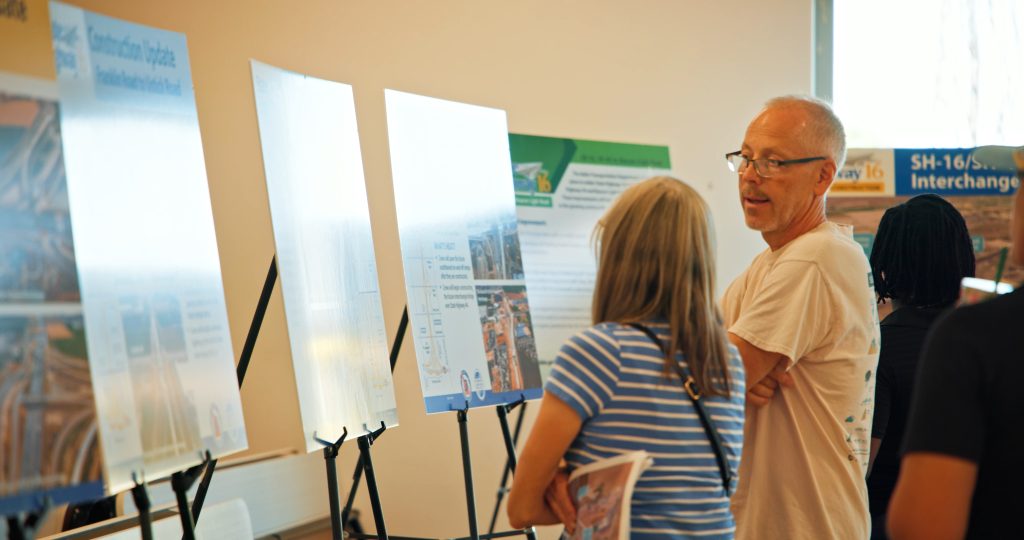 Two community members at a State Highway 16 Quarterly meeting in front of a few display boards.