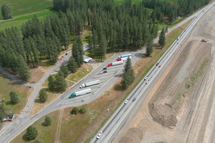 Aerial view of a large parking area with several semi-trucks parked in a line near the interstate.