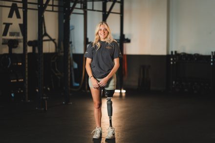Young female with a prosthetic leg standing in a gym with workout equipment in the background.